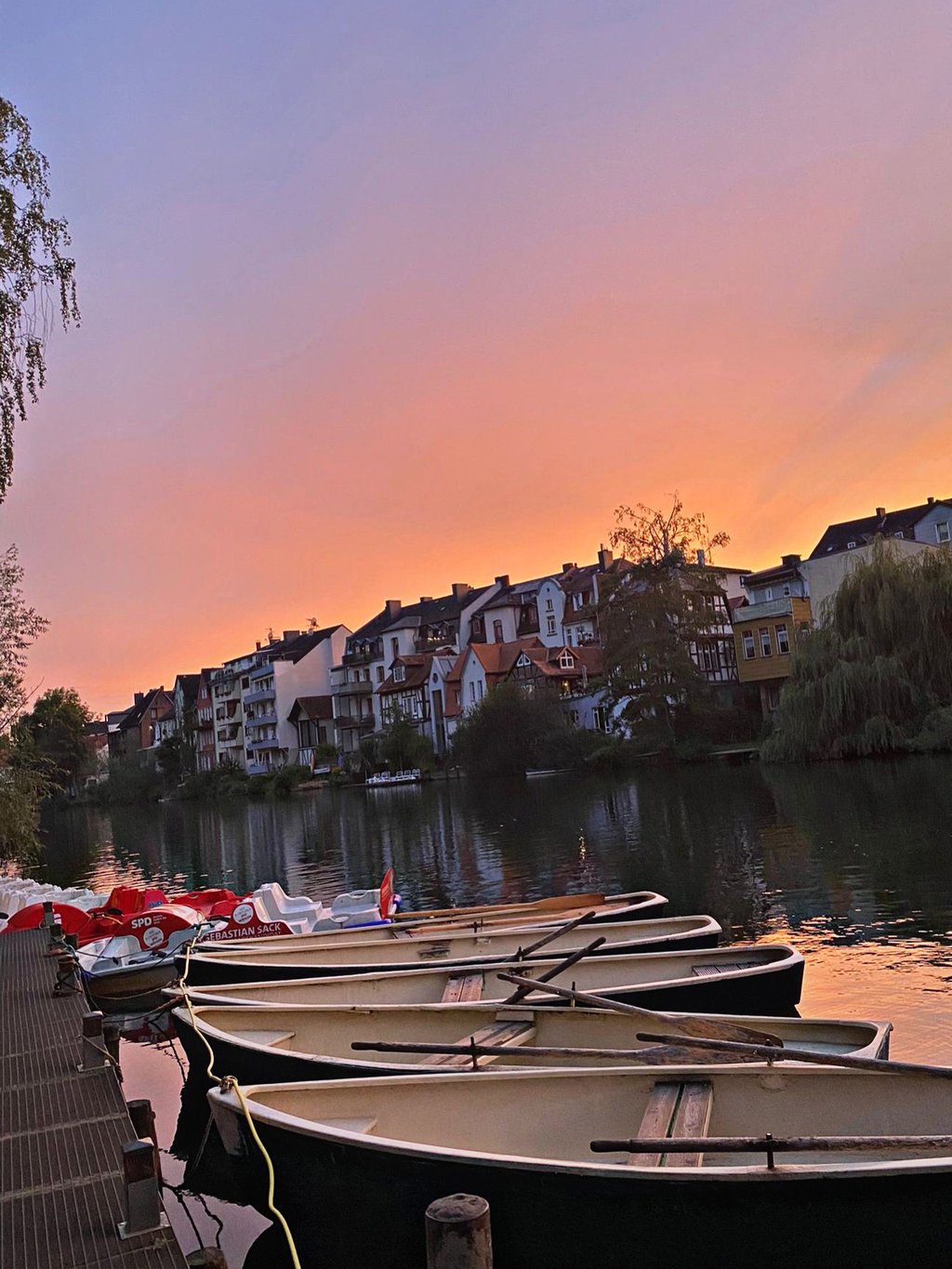 Ruderboote am Steg bei rosa-orangem Abendhimmel mit Marburger Skyline