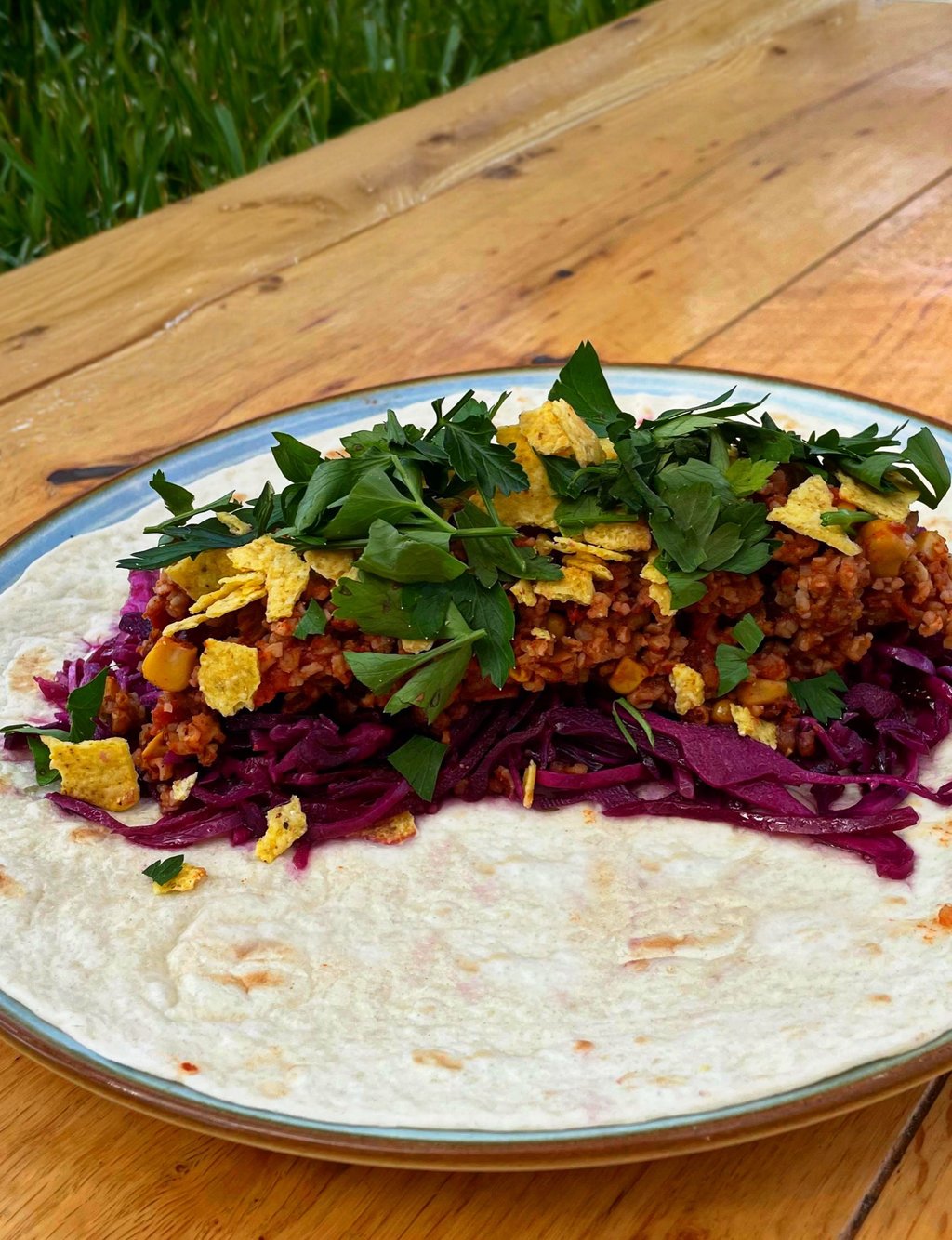 Chili-Bulgur-Wrap mit Rotkohl, Tortilla-Chips und Petersilie auf Holztisch