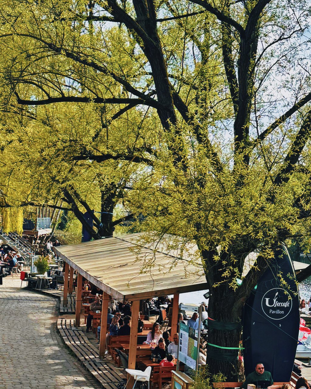 Pavillon im Frühling mit dichtem grünen Blätterdach und dinierenden Gästen