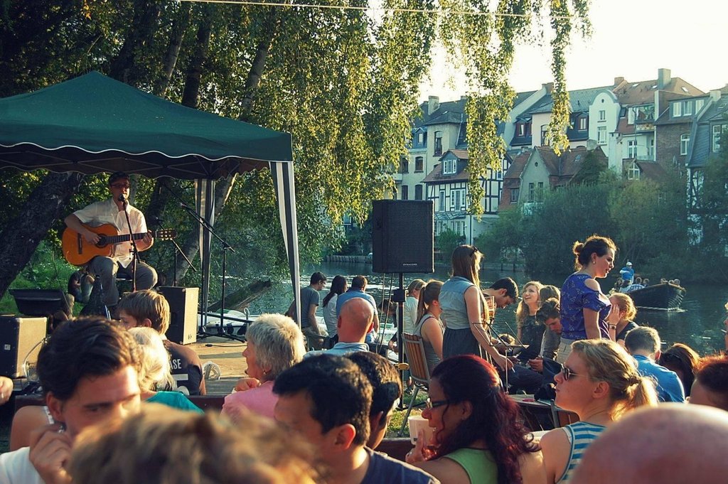 Akustik-Gitarrist spielt bei goldener Abendstunde auf der vollen Terrasse